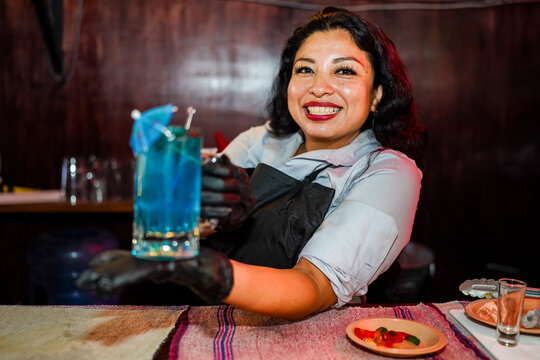 Latin woman bartender serving blue cocktail at night