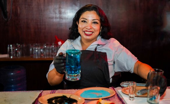 Latin woman bartender holding blue cocktail