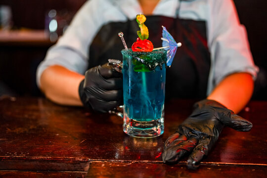 Hispanic bartender serving blue cocktail at a small business bar