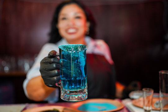 Latin woman bartender holding blue cocktail