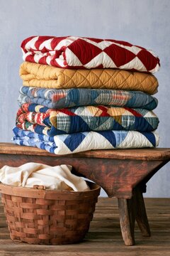 Stack of colorful quilts on wooden bench with basket for cozy home decor