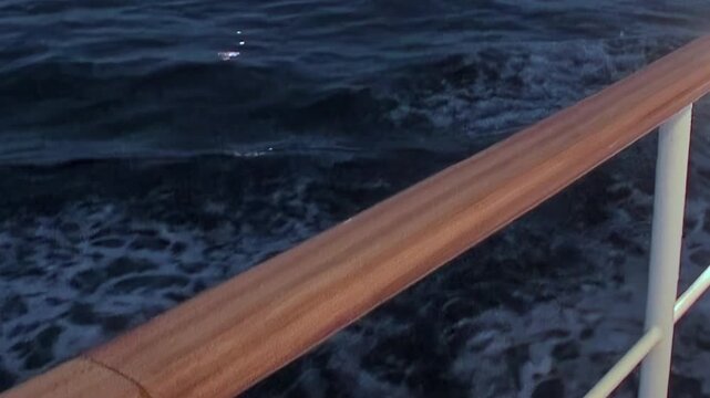 A serene view from a ship reveals the vast, deep blue waters of the Arctic Ocean. Gentle waves ripple past a polished wooden railing, capturing the essence of a tranquil polar voyage.
