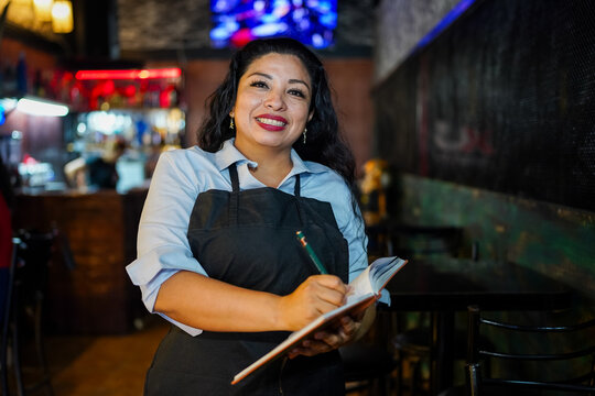 Hispanic female server smiling while taking an order in a bar