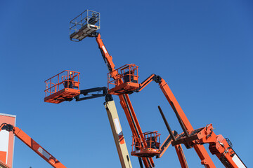 Several orange articulated lifts extend upward, forming a striking industrial scene © Aleksandr Fedosov