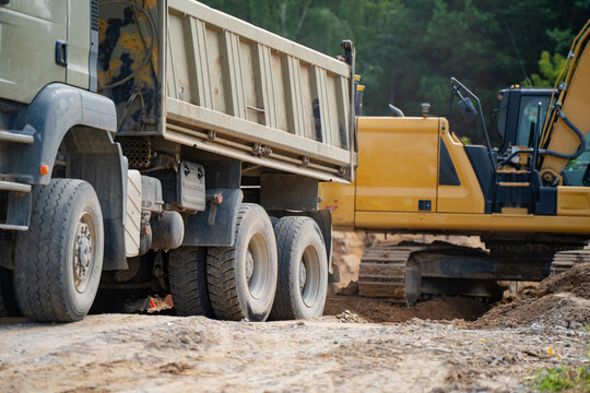 Heavy duty tipper dump truck beside tracked excavator performing subgrade excavation and earthmoving operations on construction site