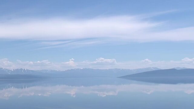 Gaze upon the tranquil expanse of Hovsgol Lake in Mongolia. Its pristine waters flawlessly mirror the vibrant azure sky and distant majestic mountains, some with snowy peaks.