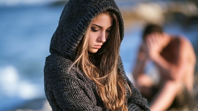 Sad young woman looking at camera with a blurry man in background