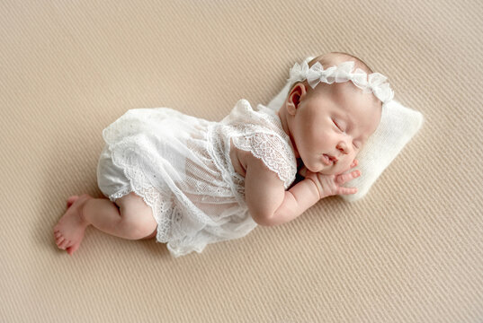 Newborn baby girl sleeping peacefully on soft fabric wearing white lace outfit during studio session