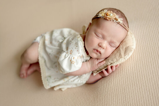 Newborn baby girl sleeping peacefully on soft fabric wearing white lace outfit during studio session