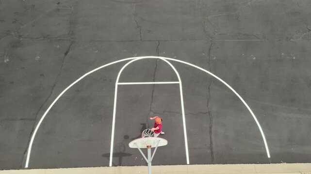 Aerial overhead view of middle-aged man shooting hoops on an outdoor basketball court for health, fitness, and active wellness at a public park