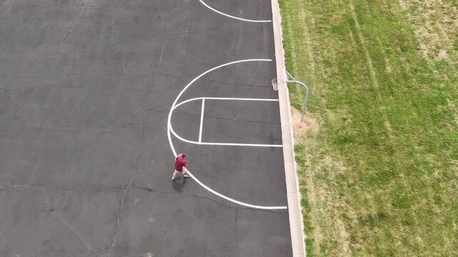 Aerial overhead view of middle-aged man shooting hoops on an outdoor basketball court for health, fitness, and active wellness at a public park