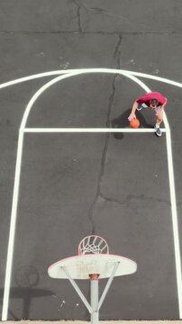Aerial overhead view of middle-aged man shooting hoops on an outdoor basketball court for health, fitness, and active wellness at a public park