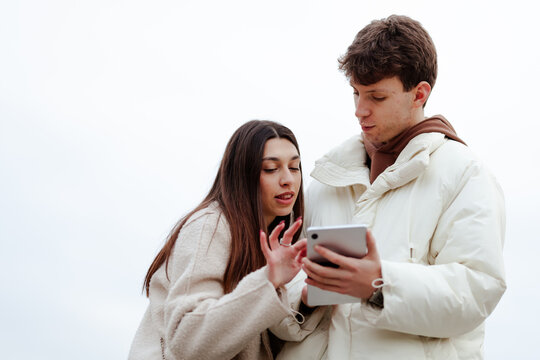 Young couple looking at a tablet while outdoors wearing winter clothing, demonstrating interest and concentration