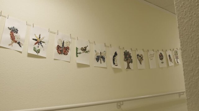 Nature drawings by children hanging on a clothesline indoors