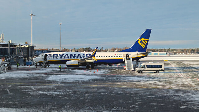 Ryanair passenger aircraft parked at Riga International Airport with mobile stairs, airport bus and ground crew on snowy winter apron: Riga, Latvia - January 13, 2025