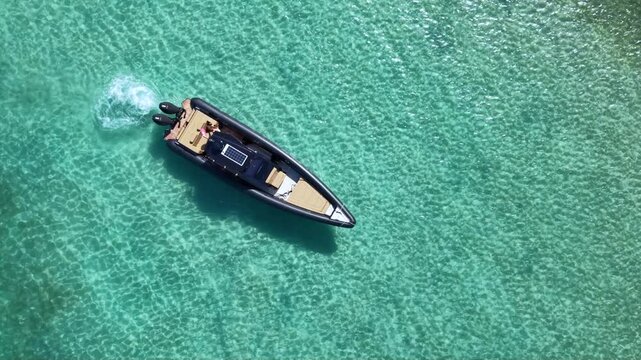 Top-down aerial view of a luxury inflatable motorboat floating over crystal clear turquoise sea, with visible seabed patterns and large copy space creating an idyllic summer travel scene.