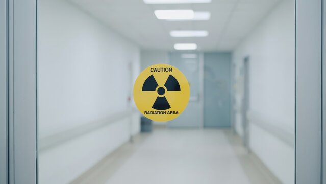 Radiation area caution sign on glass door, yellow radioactive hazard symbol in hospital hallway, medical laboratory safety warning