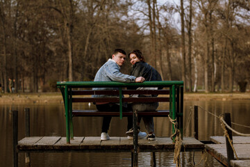 Fototapeta premium Couple enjoys a quiet moment together on a bench by the water during a sunny day in a tranquil park setting