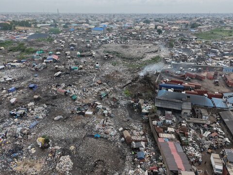 Lagos, Nigeria - 01 August 2026: Aerial view of Abule Egba, showing the sprawling landfill site with makeshift shelters, smoke rising from waste, and industrial trucks in Lagos.