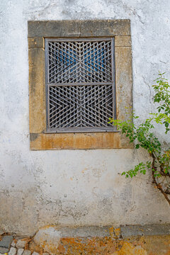 Traditional wooden lattice window detail on an ancient stone wall in the historic village of Obidos, Portugal.