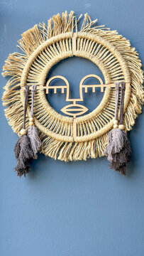 Handcrafted boho wall decoration made of natural rope with an abstract wooden face, tassels and fringe displayed on a blue wall, modern bohemian interior decor.