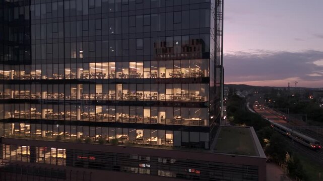 Aerial View of Modern Office Glass Facade with Illuminated Workspaces and Railway at Sunset for Corporate Business