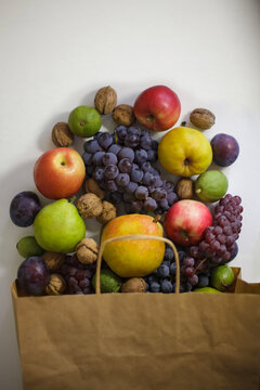 Fresh organic autumn fruits spilling from paper bag on white surface with copy space