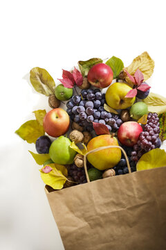 Fresh autumn fruits spilling from craft paper bag on white surface with copy space