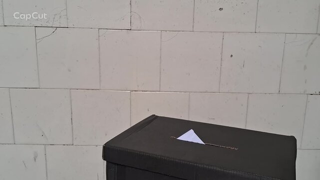 Voting hand inserting white paper ballot into black box video footage