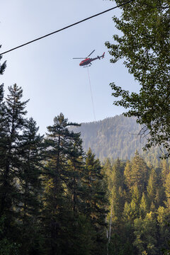 Red Helicopter Carrying Sling Load Over Forested Mountain Valley With Smoke From Wildfires Near Hope, BC