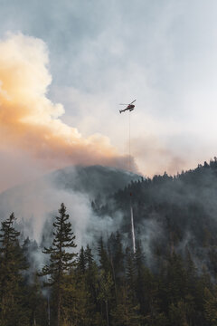 Firefighting Helicopter Dropping Water Over Smoky Forest Wildfire Near Hope, BC, Canada At Dusk