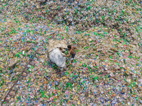 Chattogram, Bangladesh - 25 April 2026: Aerial view of a worker collecting plastic bottles from a massive waste pile in a recycling facility.