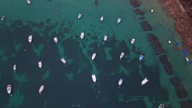 Top-down drone overview of numerous small private boats and motorboats anchored across clear turquoise coastal water at Saint-Lunaire, Bateaux, Brittany, France