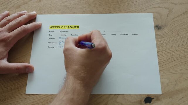 A person fills out a weekly planner to organize tasks, appointments, and goals. Concept of time management, productivity, planning, and personal organization.