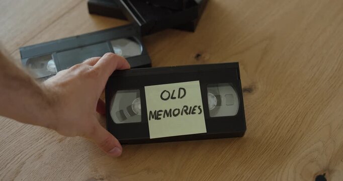 Hand placing a "MEMORIES" label on an old VHS cassette tape. Ideal for nostalgia, family memories, home videos, analog media, archives, and video digitization concepts.