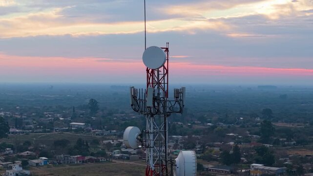 Telecommunications tower with multiple antennas overlooks San Jose de Feliciano and rural outskirts in Feliciano, Entre Rios, Argentina, during evening light, orbiting.
