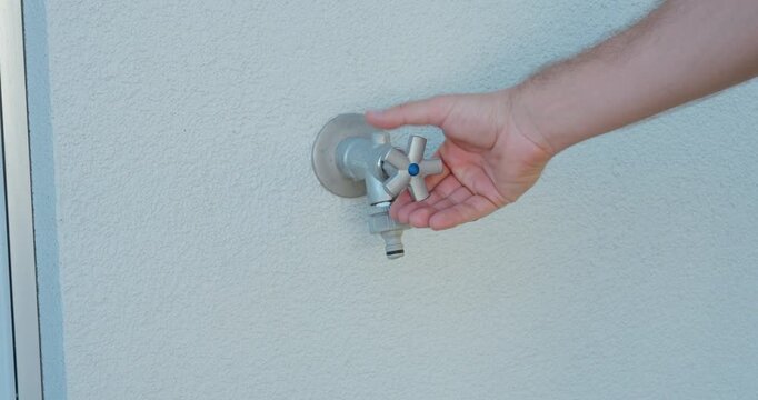 Hand opening an outdoor tap with no water coming out. Ideal for water shortage, drought, water scarcity and climate change concepts.