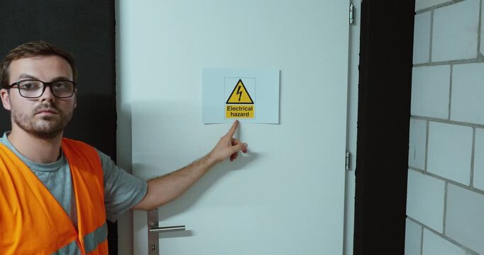 Worker attaching an electrical hazard warning sign to a door. Ideal for electrical safety, workplace hazards and accident prevention.