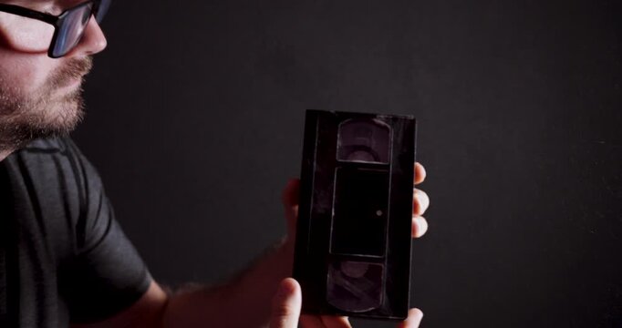 Man blowing dust off an old VHS cassette. Ideal for nostalgia, retro technology, forgotten memories, archives and vintage media.