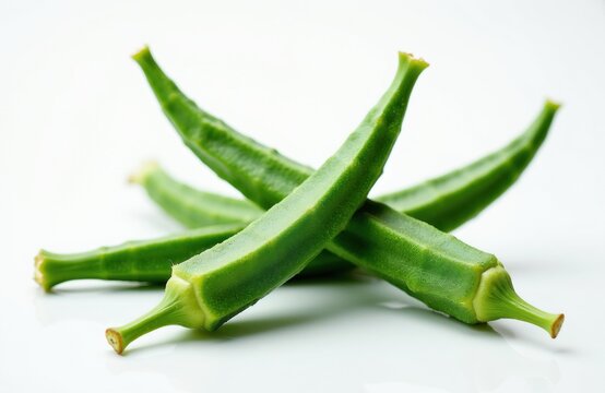Three vibrant green okra pods lie on clean white surface. Fresh raw vegetables display textured skin with edible stems. Healthy organic produce ingredient creates culinary pattern. Close up food