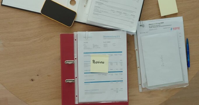Applying a review sticky note to business documents for later verification. Ideal for office organization, document management, accounting, and workflow concepts.