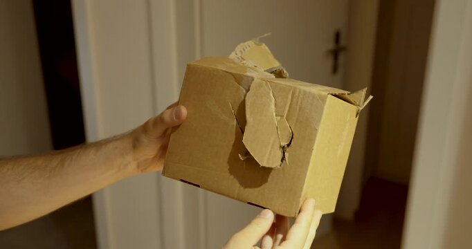 Man holding a badly damaged cardboard package. Ideal for shipping damage, delivery problems, logistics, complaints and parcel insurance.