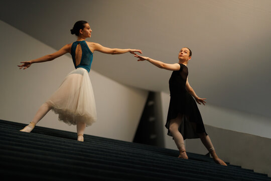 Two ballet dancers performing an elegant partnered pose on a modern staircase during rehearsal under soft architectural lighting