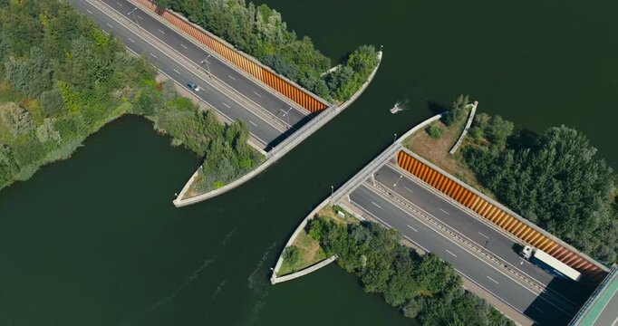 Drone orbits the iconic Veluwemeer Aqueduct near Harderwijk, revealing a boat crossing above while cars drive beneath on a sunny day in the Dutch countryside.