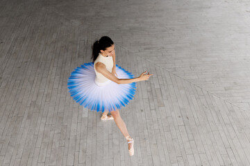 Ballet dancer practicing on pointe in a blue and white tutu, photographed from above on a textured wooden dance floor © Nikola Spasenoski