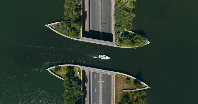 Beautiful top-down drone view of the iconic Veluwemeer Aqueduct near Harderwijk, with a boat crossing above while cars, trucks and cyclists pass beneath on the provincial road.
