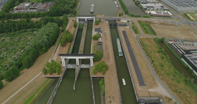 High aerial drone view of cargo boats waiting in a Dutch canal lock for the gate to open, while cars cross the road above the river, highlighting inland shipping and water management infrastructure.