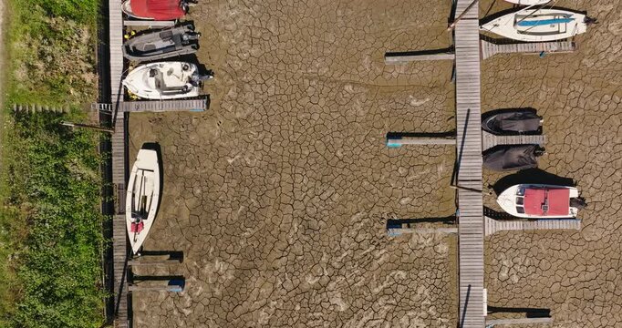 Aerial top down view of boats stranded in a dried harbor with extremely low water levels, exposing cracked soil and highlighting drought, water scarcity and climate change.
