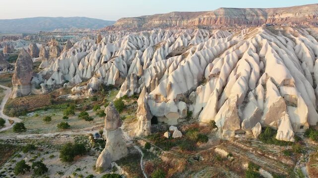 Panoramic aerial drone view of iconic fairy chimney rock formations and steep eroded tuff mountain ridges in Love Valley, Cappadocia, Nevsehir, Turkey during golden hour.