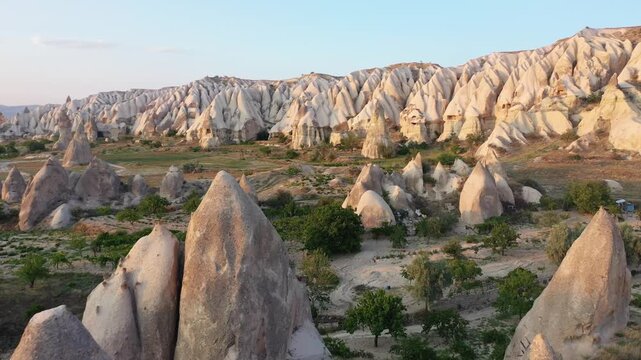 Panoramic aerial drone view of iconic fairy chimney rock formations and steep eroded tuff mountain ridges in Love Valley, Cappadocia, Nevsehir, Turkey during golden hour.